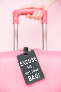 Person s hand holding handle travel suitcase with your bag tag against pink background