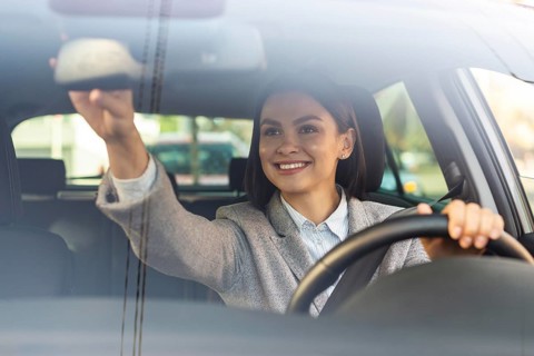 Smiley businesswoman adjusting her car s rear view mirror