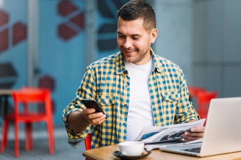 Man with laptop using smartphone cafe