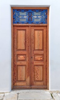 Old vintage wooden house doors in light natural color decorated with blue forge-smithing metal ornament with monograms of capital letters M and X. Whitewashed walls