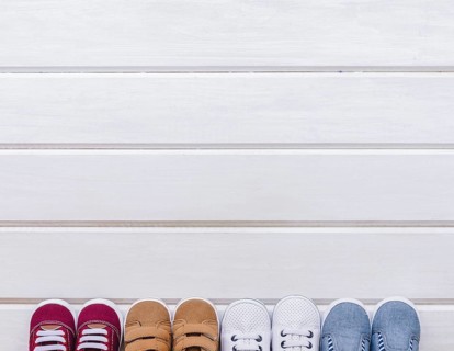 Baby concept with four pairs shoes space wooden surface