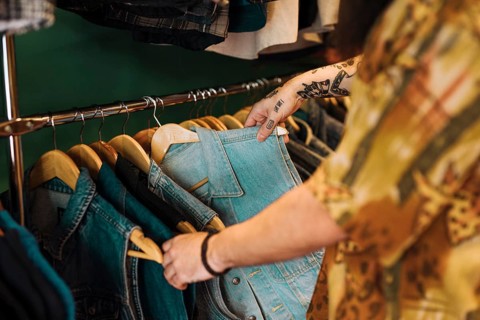 Close up man s hand choosing blue jacket hanging rail clothing shop
