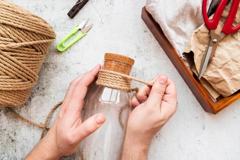 Close up person wrapping jute string glass bottle white textured backdrop
