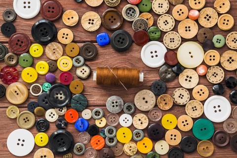 Many colorful buttons brown thread needle wooden background