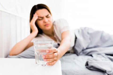 Female suffering from headache taking glass water