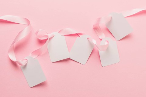 Overhead view blank tags pink ribbon against plain pink backdrop