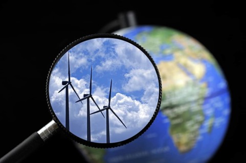 Wind farm turbines against cloudy sky seen through magnifying glass held against illuminated terrestrial globe