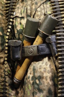 Close up of two WW2 stielhandgranaten tucked under pants belt of German SS soldier carrying machine gun ammunition belt