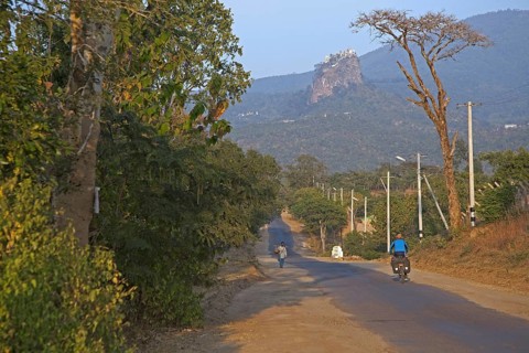 Tourist cycling towards Buddhist monastery on the summit of Taung Kalat near the volcano Mount Popa