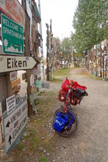 Various traffic and place signs face a bicycle loaded with luggage