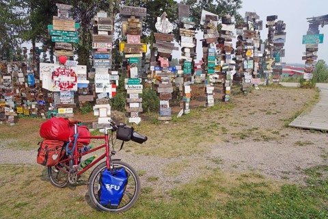 Various traffic and place signs face a bicycle loaded with luggage