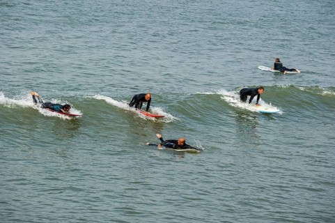Surfers in wetsuits riding wave on surfboards as it breaks at sea