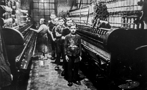 Old black and white archival photograph showing female worker and child labourers posing in spinning mill in the early twentieth century