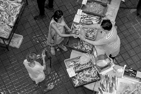Black and white bird's eye view photo of a stall full of fish with the seller and a buyer