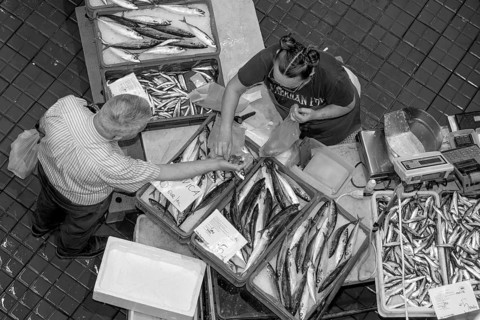 Black and white bird's eye view photo of a stall full of fish with the seller and a buyer