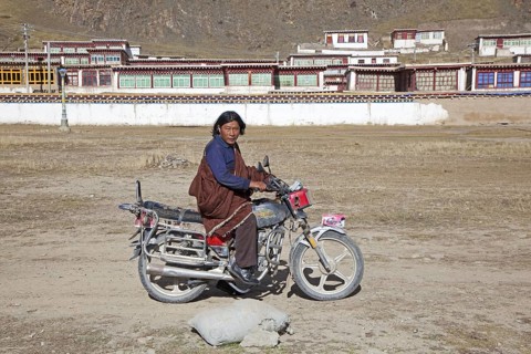 Tibetan man riding motorbike in front of monastery between Sershu Dzong and Sershu