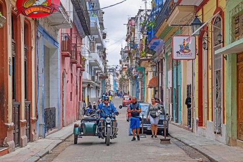 Cubans and motorcycle with sidecar in narrow street with bars and restaurants in the colonial city centre Old Havana