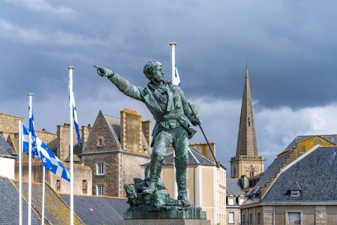 Statue of the privateer Robert Surcouf in front of the old town with the tower of St Vincent Cathedral