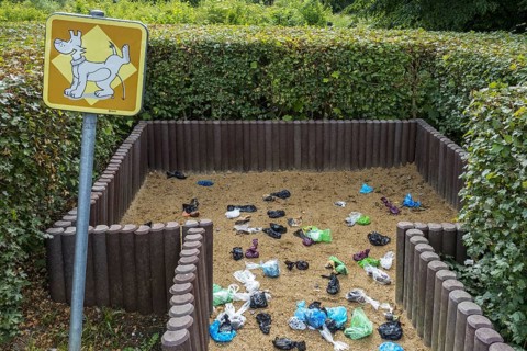 Fenced sandy public dog toilet area in city park filled with colourful discarded plastic dog poop bags