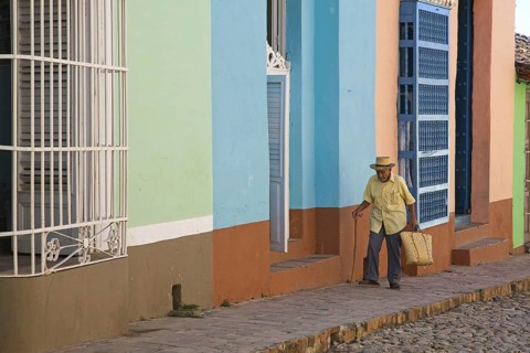 Old Cuban man walking along pastel coloured houses with barrotes and grilles in Trinidad