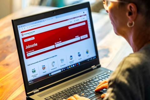 Woman with glasses looking for a job sits at home in front of her notebook and checks the internet site of the Federal Employment Agency for job offers