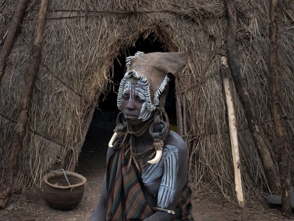 Woman from the Mursi tribe with headdress and face painting in front of her hut