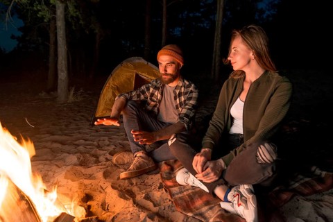 Couple warming up night by campfire