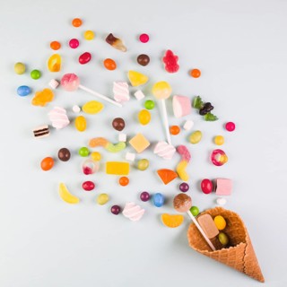 Elevated view various candies with ice cream waffle cone white background