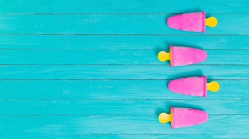 Bright pink frozen popsicles yellow sticks wooden background