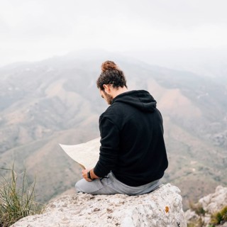 Male hiker sitting top rock looking map