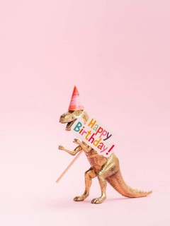 Funny toy dinosaur holding happy birthday sign