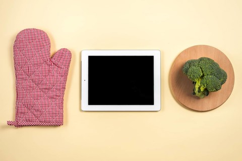 Mitt oven glove digital tablet broccoli wooden tray against beige background