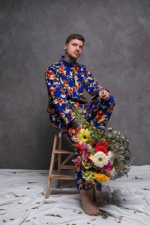 Thoughtful young man sitting wooden small ladder holding flower bouquet hand