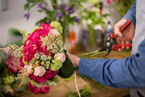 Male florist cutting colorful flower bouquet twigs with pruning shears