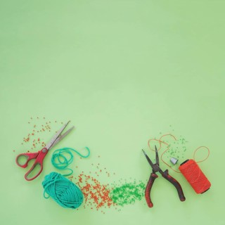 Scissor plier wool beads orange yarn spool green background