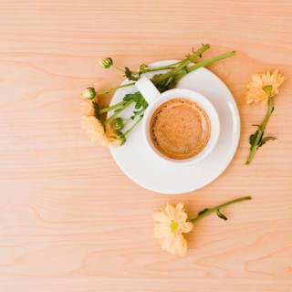 Overhead view coffee cup saucer with peach colored flowers wooden textured background