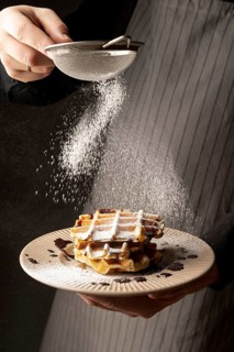 Front view man coating waffles with powdered sugar