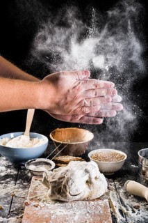 Close up baker s hand dusting flour dough with ingredients table