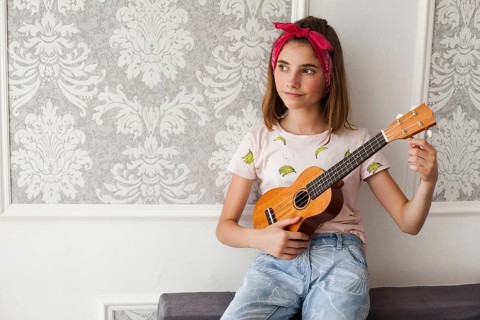 Smiling girl sitting sofa adjusting ukulele thinking