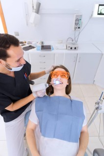 Happy male dentist checking patient s teeth with dental uv light equipment clinic