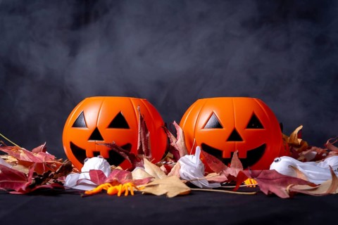 Halloween pumpkins over red autumn leaves and ghosts with smoke on a black background