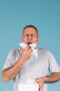 Senior man holding tissue paper about sneeze blue background