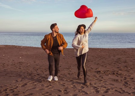 Happy couple running sea shore with heart balloons