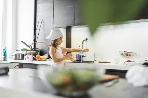 Girl with chef hat washing her hand faucet home