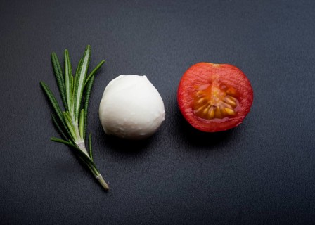 Green rosemary half cheery tomato mozzarella cheese black surface