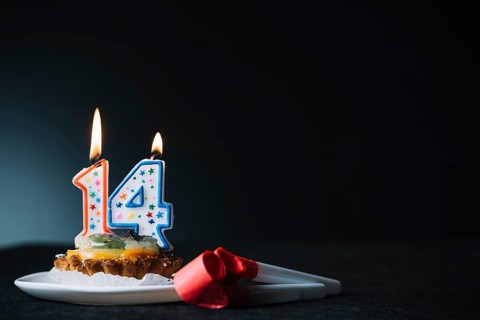 Number 14 birthday lighted candle slice tart party horn blower against black backdrop