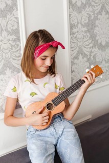 Smiling little girl playing ukulele home