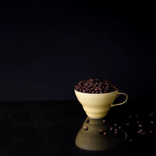 Ceramic cup filled with roasted coffee beans black background