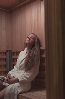 Woman white bathrobe sitting wooden bench relaxing sauna