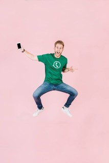 Excited man with smartphone jumping pink backdrop